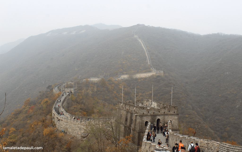 Vista panorámica de la Gran Muralla China en una colina neblinosa, con visitantes caminando por el sendero.