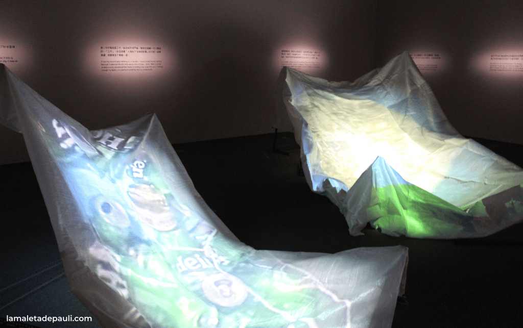 Instalación artística con proyecciones en telas translúcidas que crean formas y colores dinámicos en un entorno de exposición.