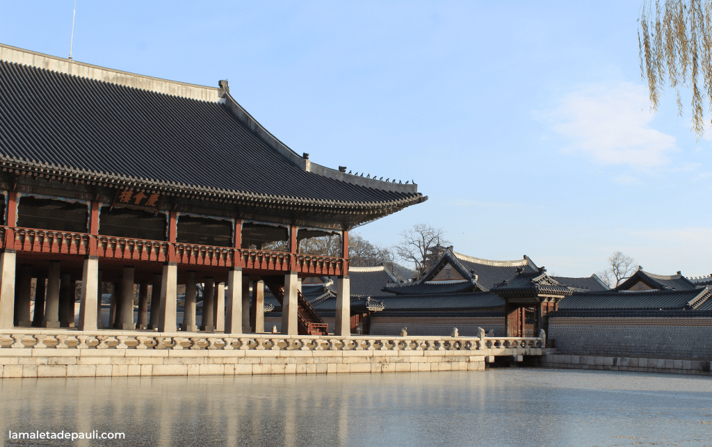 Vista de un palacio tradicional coreano con un lago reflejante y un cielo azul despejado.