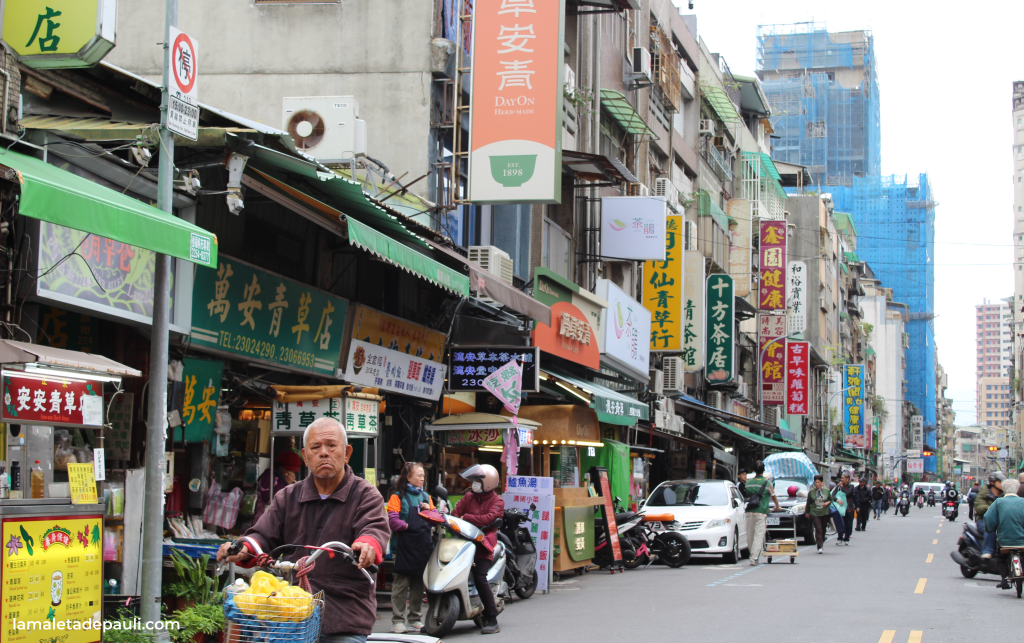 Calles concurridas de un mercado en una ciudad, con tiendas y restaurantes locales, y personas caminando y en scooters.